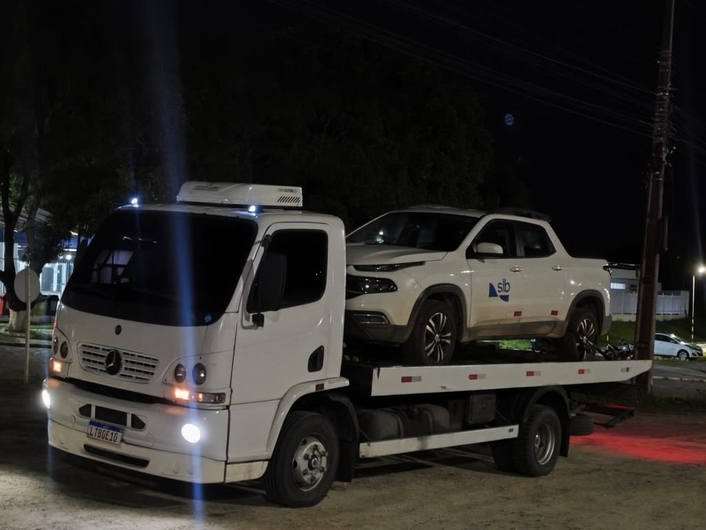 Atendimento noturno com picape branca sobre caminhão plataforma